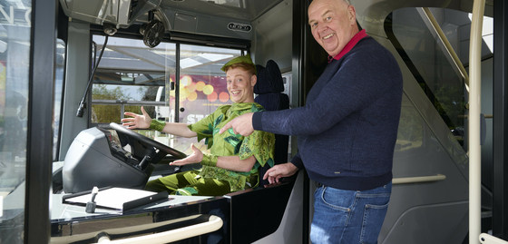 Peter Pan is sat at the driver's seat on a D&E Coach, with Donald from the company stood beside him, pointing to the wheel.