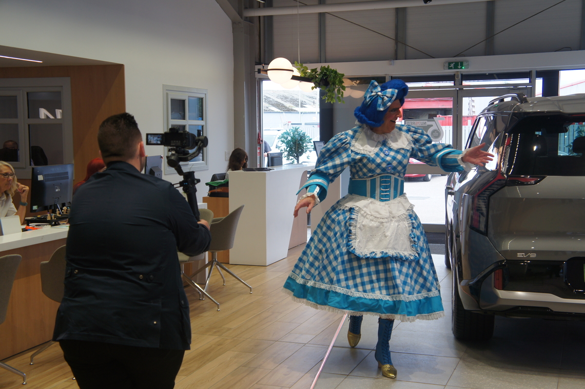 Dame Moira walks around a car at Dicksons, while being filmed by their digital team