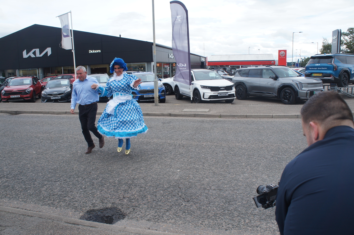 Dame Moira and Innes from Dicksons crosses the road outside their showroom, while their photography team takes a photo of them.