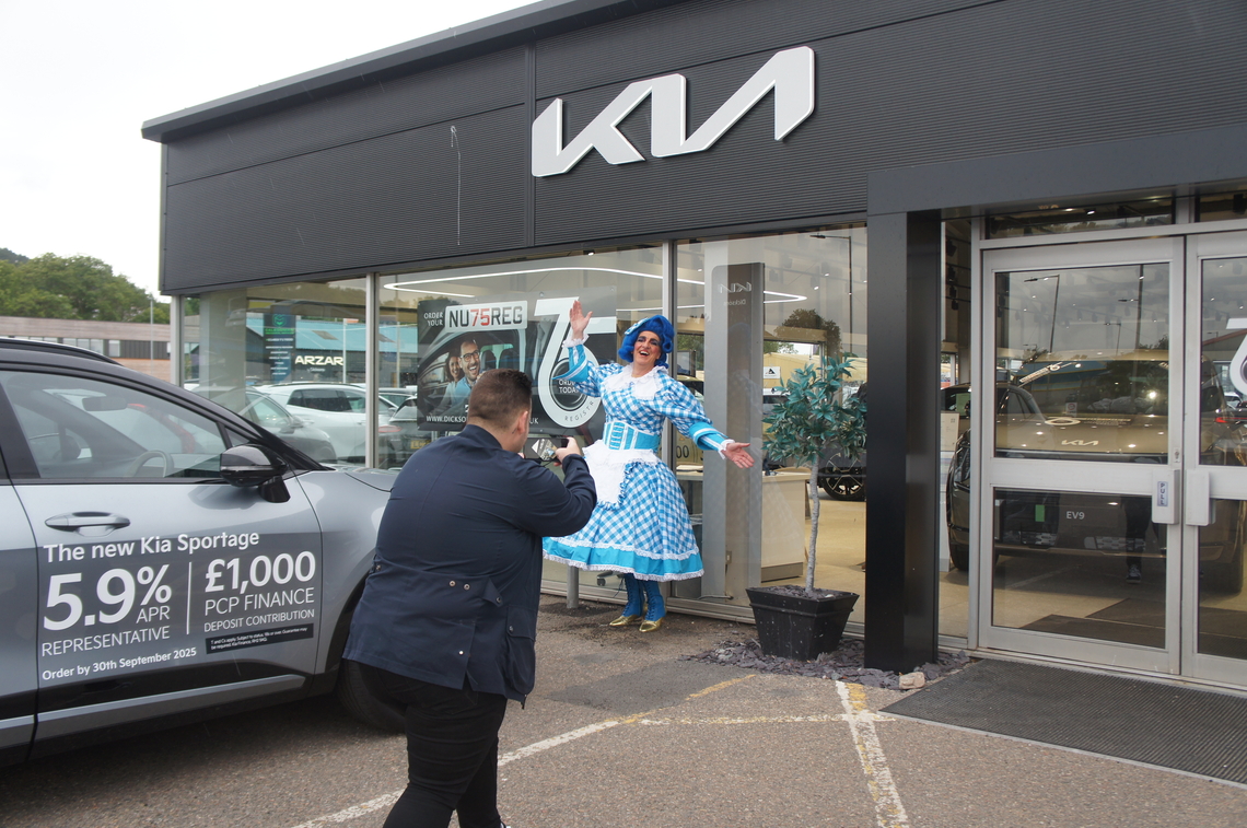 Dame Moira stands in front of Dicksons of Inverness showroom, while being photographed by their photography team.
